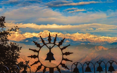 Panoramic view of snow-capped Himalayan peaks, including Nanda Devi, visible through a bell frame